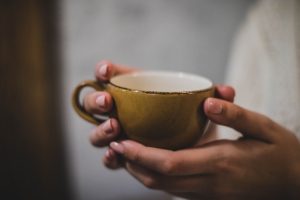 Woman holding cup of coffee. Things to stop doing when struggling with money.