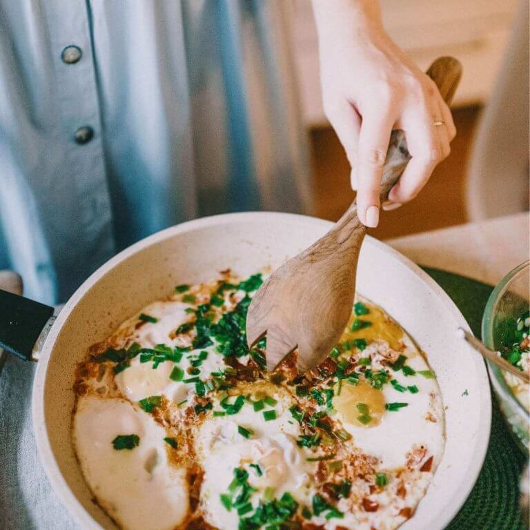 Woman in blue dress cooking eggs in frying pan with wooden spoon. 10 tips to feed your family for less